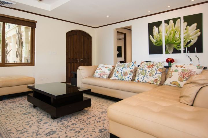 Living room with beige sofas, floral pillows, dark wood table, and plant artwork on wall.