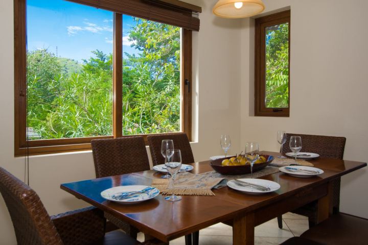 Dining table set for four near windows with a view of greenery outside.