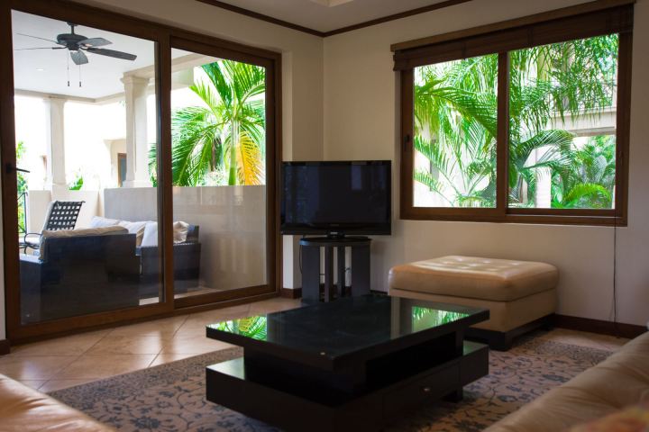 Living room with TV, glass table, sliding doors, and garden view.
