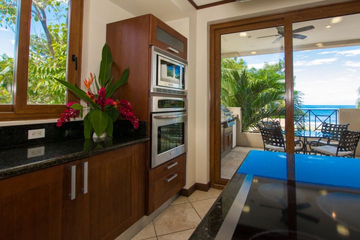 Modern kitchen with wood cabinets, built-in oven, and ocean view from a glass door leading to a patio.