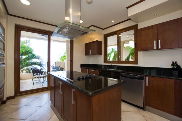 Modern kitchen with wooden cabinetry, island, and glass doors leading to a patio with outdoor seating.