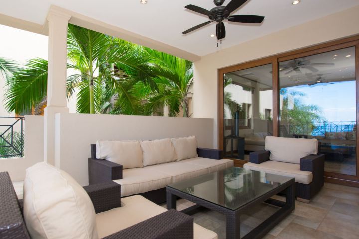 Outdoor patio with wicker furniture, glass table, ceiling fan, and tropical plants nearby.