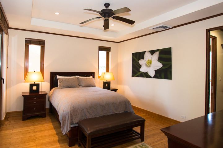 Bedroom with a bed, nightstands, lamps, a ceiling fan, and a flower painting on the wall.