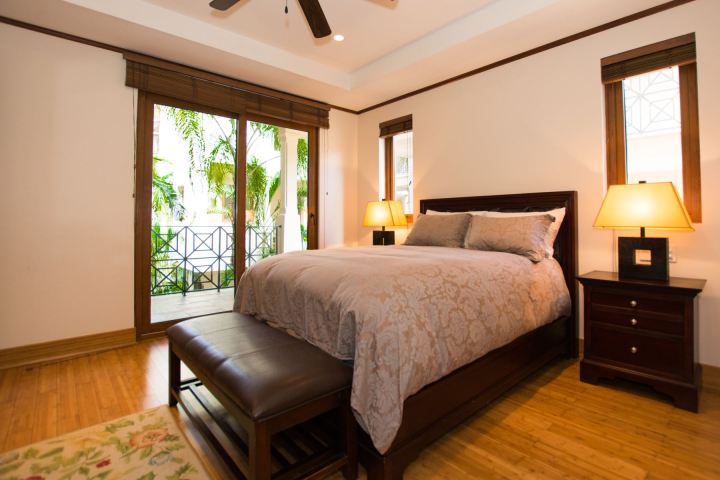 Cozy bedroom with a double bed, two lamps, wooden floors, and a balcony view with plants.