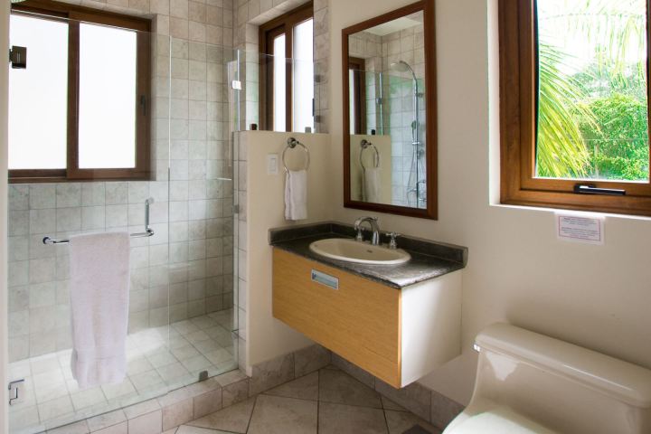 Modern bathroom with glass shower, sink, and window with greenery outside.
