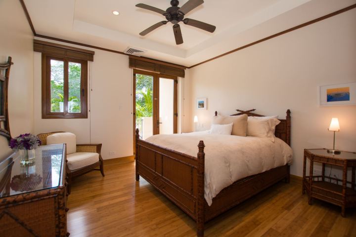Cozy bedroom with wooden furniture, large bed, ceiling fan, and balcony view.