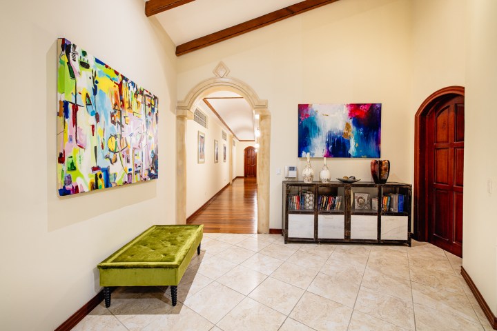Hallway with colorful paintings, green bench, and bookshelf with decor and books.