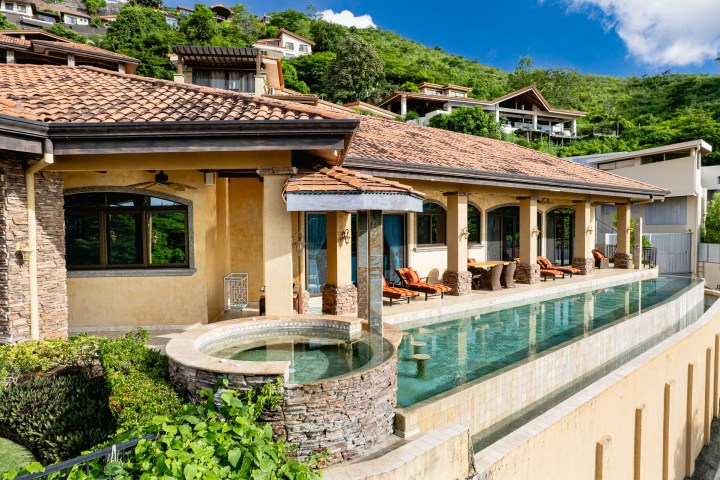 Luxury villa with infinity pool, arched windows, and hillside view.