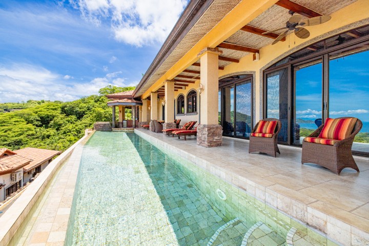 Luxurious villa with infinity pool, wicker chairs, and scenic forest view.