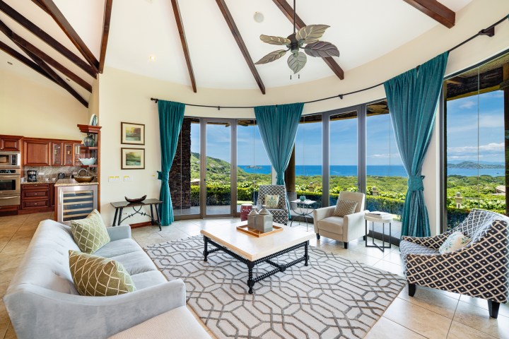 Spacious living room with ocean view, ceiling fan, teal curtains, and elegant furniture.