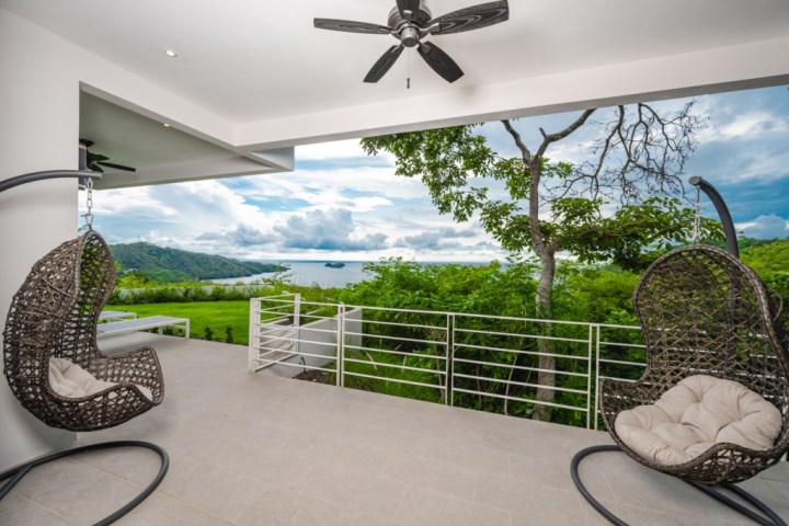Outdoor patio with hanging chairs, ceiling fan, and ocean view.
