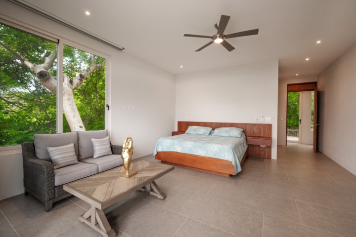 Minimalist bedroom with a bed, sofa, coffee table, and window view of trees.