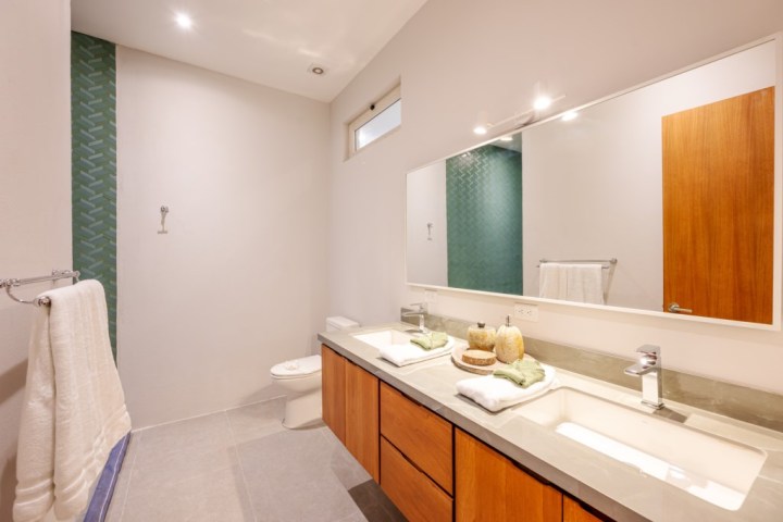 Modern bathroom with dual sinks, large mirror, toilet, and green tiled wall.
