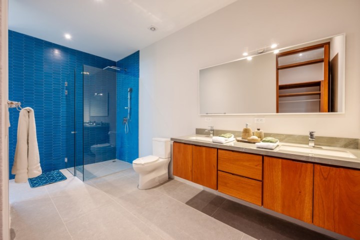 Modern bathroom with blue-tiled shower, double sinks, and wooden cabinets.