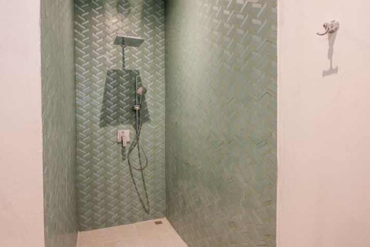 Shower with green herringbone tiles and silver fixtures against white walls.
