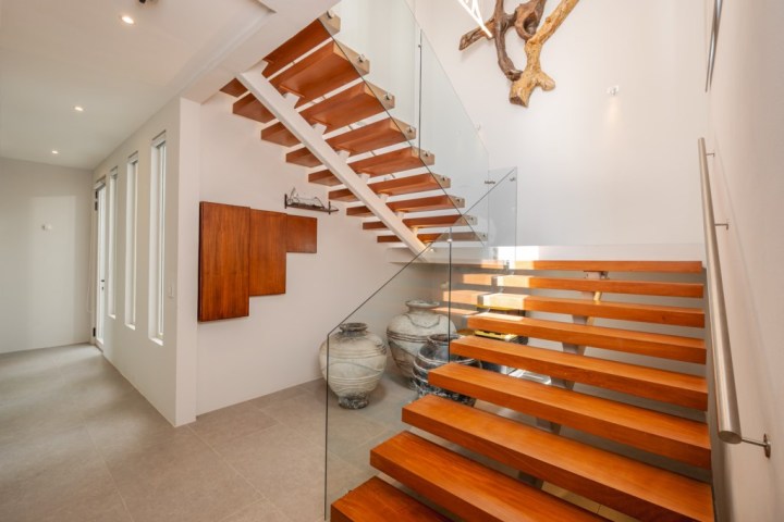 Modern wooden staircase with glass railing, wall art, and decorative pottery jars.