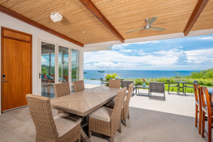 Outdoor patio with wicker chairs, table, ocean view, and ceiling fan.