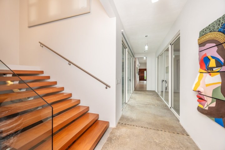 Modern hallway with wooden stairs, glass railing, and colorful face artwork on the wall.