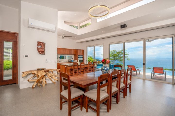 Modern dining room with wooden table, ocean view, and large windows.