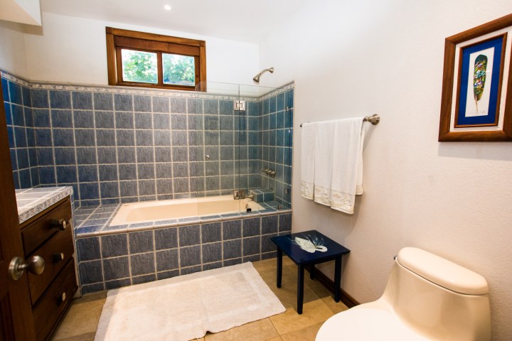 Bathroom with blue-tiled bathtub, white towel, small table, and wall art.