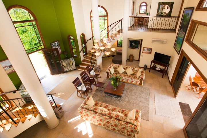 Spacious living room with green wall, floral sofas, staircase, and large windows.