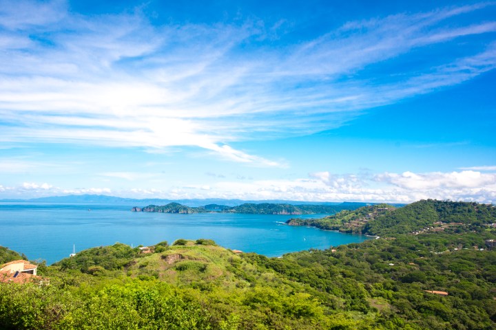 Scenic coastal landscape with green hills, blue ocean, and a bright sky with clouds.