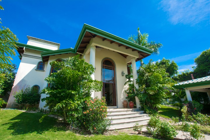 Elegant house with green roof and stairway surrounded by lush plants.