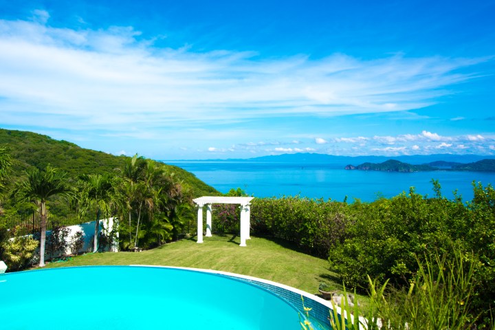 Infinity pool overlooking ocean and hills under a clear blue sky.