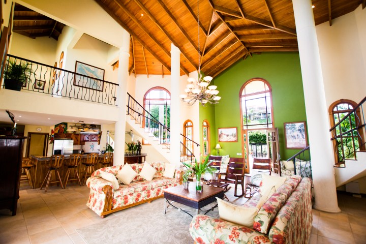 Spacious living room with high ceiling, floral sofas, wooden furniture, and green accent wall.