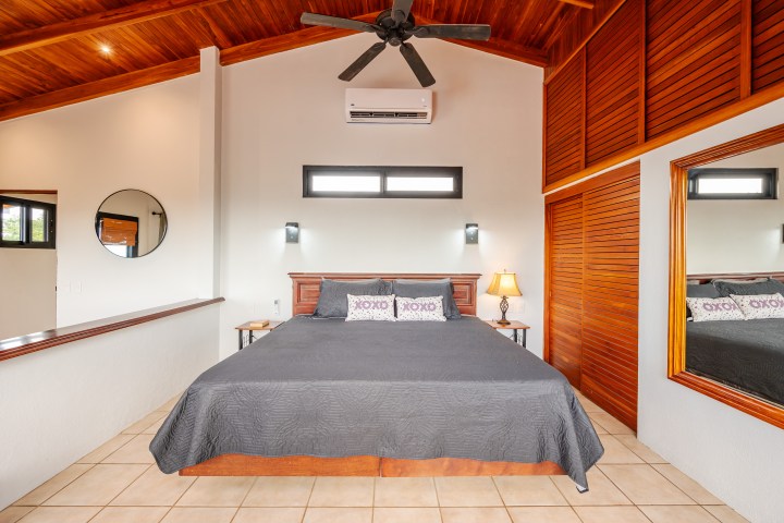 Bedroom with a king bed, wooden ceiling, fan, mirror, lamp, and air conditioning unit.