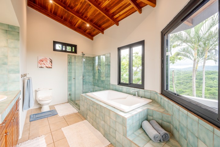 Modern bathroom with bathtub, glass shower, and large window view of trees.