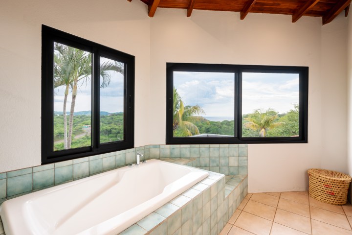 Bathroom with a bathtub and large windows showcasing a scenic outdoor view with trees and sky.