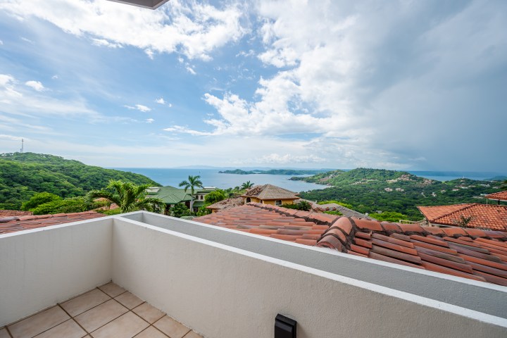 Balcony view of ocean and green hills under a partly cloudy sky.