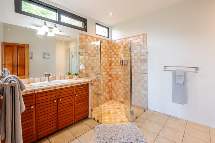Spacious bathroom with a wooden vanity and glass-door shower on tiled floor.