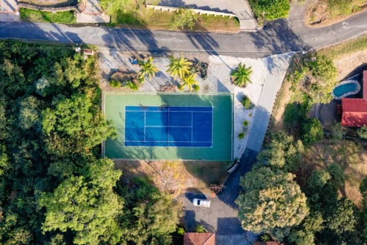 Aerial view of a tennis court surrounded by trees and a few buildings.