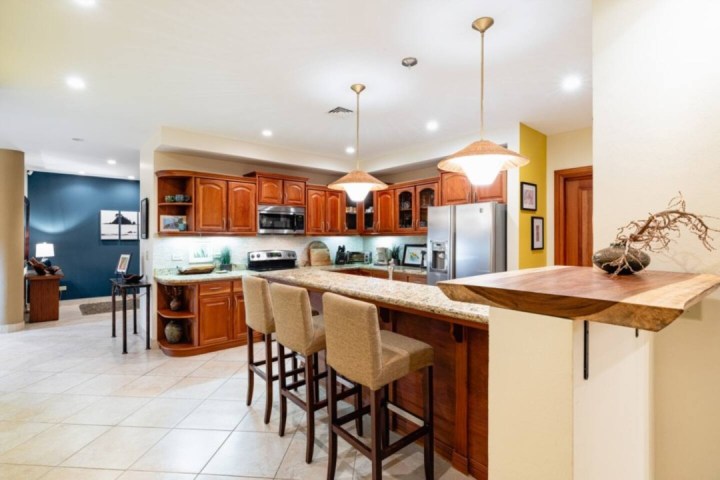Spacious kitchen with wooden cabinets, bar stools, and pendant lights over a granite countertop.