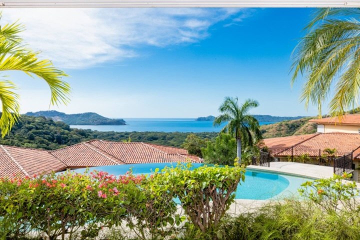 View of ocean and mountains from a terrace with pool and palm trees.