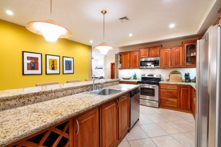 Modern kitchen with granite countertops, stainless steel appliances, and wooden cabinets, under warm lighting.