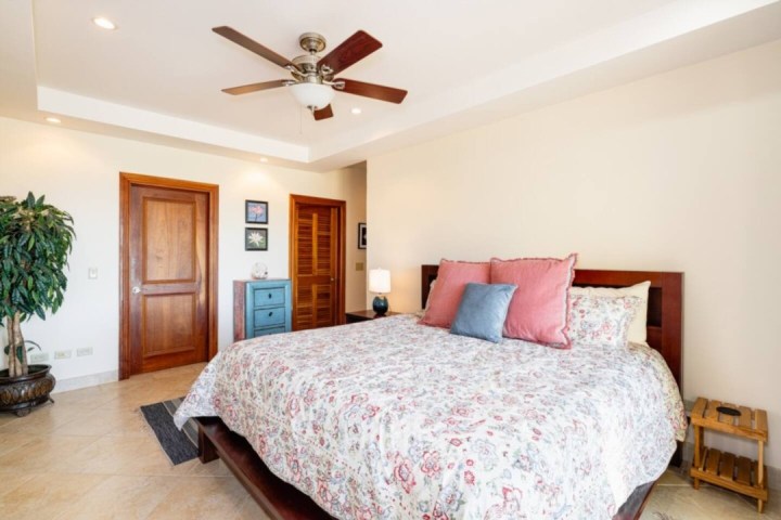 Bedroom with floral bedspread, wooden doors, ceiling fan, and a blue dresser.