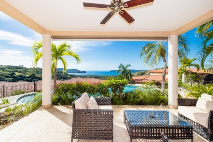 Outdoor patio with wicker furniture, ceiling fan, ocean view, and palm trees.