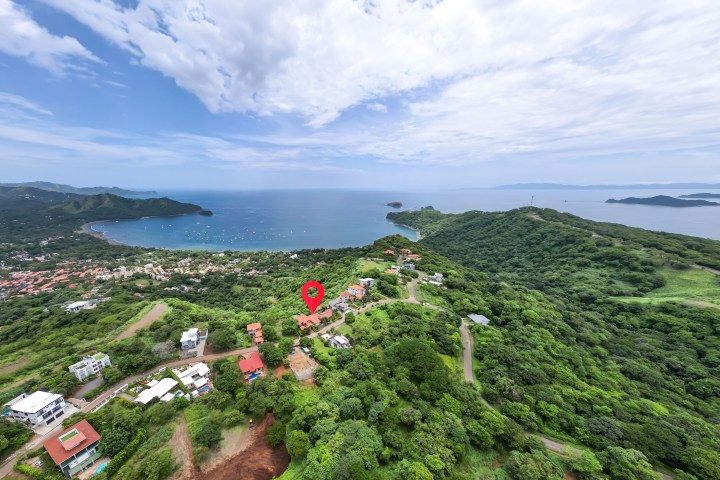Aerial view of a coastal town with lush greenery, hills, and a bay with boats.