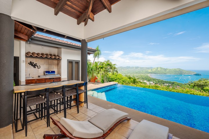 Outdoor kitchen and seating area overlooking infinity pool with ocean view.
