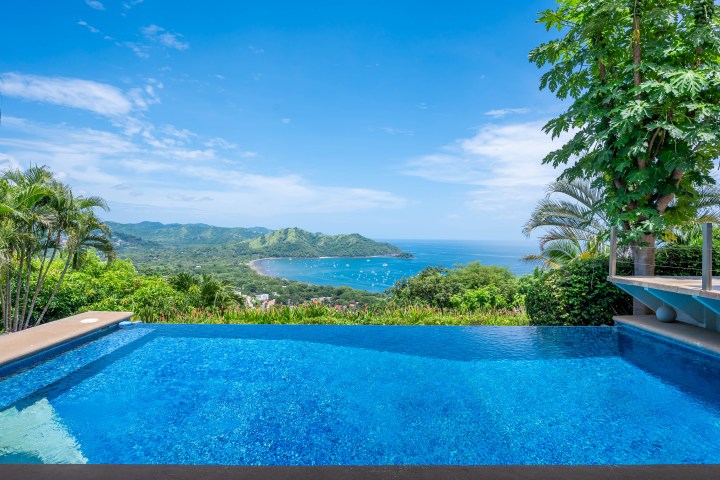 Infinity pool with view of lush hills and bay under a clear blue sky.
