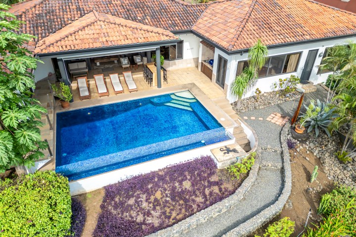 Aerial view of a house with terracotta roof, pool, and garden path.