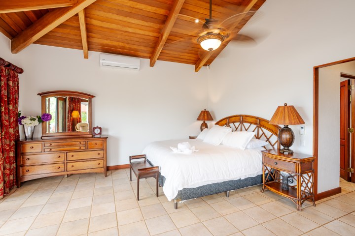 Bedroom with wooden ceiling, double bed, nightstands, dresser, and red curtains.