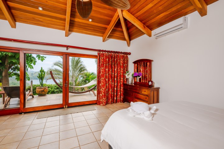 Tropical bedroom with wooden ceiling, hammock outside, and decorative swan towels on bed.