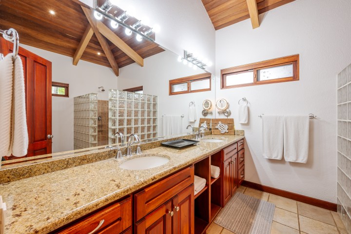Bathroom with double sink, granite countertop, wood cabinets, mirror, and glass block shower.
