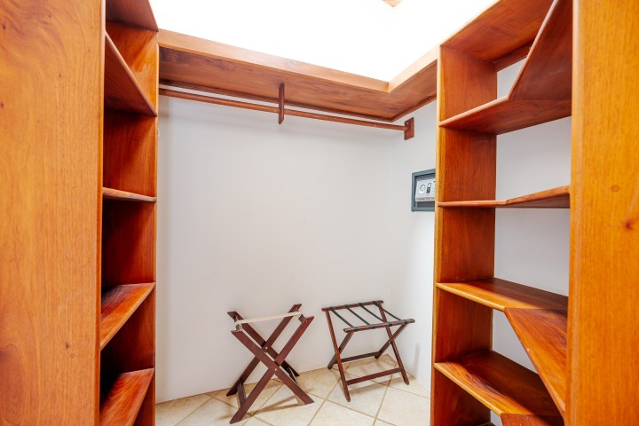 Walk-in closet with wooden shelves and hangers, two luggage racks, and a small wall safe.