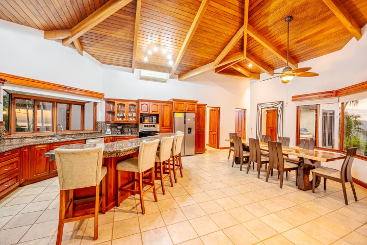 Spacious kitchen with wooden ceiling, island, bar stools, dining table, and large windows.
