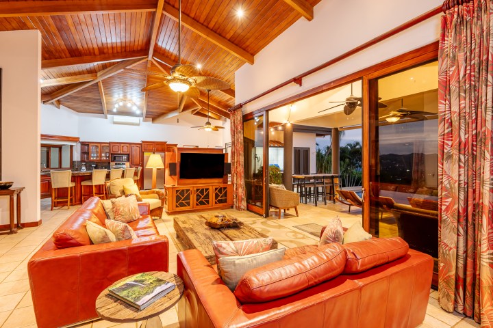 Spacious living room with red sofas, wooden ceiling, and open patio view at dusk.